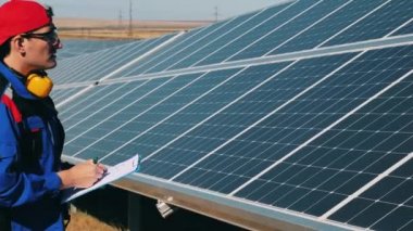 Güneş enerjisi mühendisi bir güneş enerjisi tesisinde güneş panellerini kontrol ediyor.