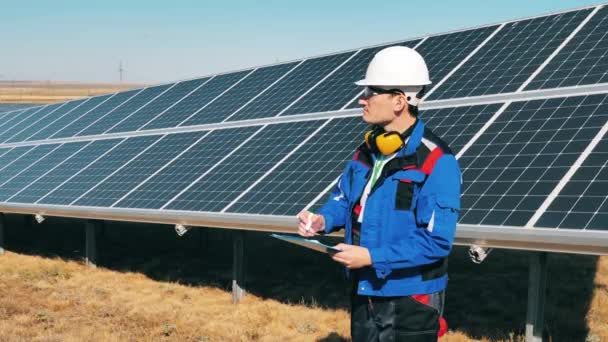 Специалист по солнечной энергии отслеживает солнечную ферму с помощью своего планшета — стоковое видео