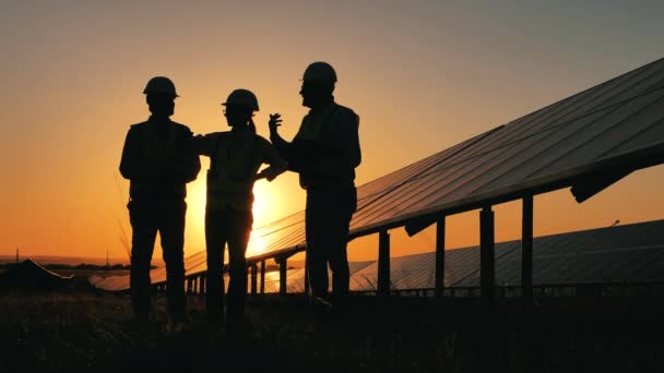 Silhuetas de três engenheiros de energia em pé em uma fazenda solar — Vídeo de Stock