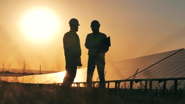 Två solenergispecialister tar en multimeter avläsningar vid solnedgången — Stockvideo