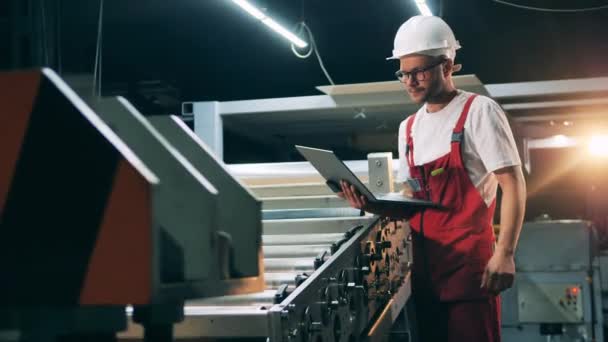 Side view of engineer watching metal working process and typing on laptop — Stock Video