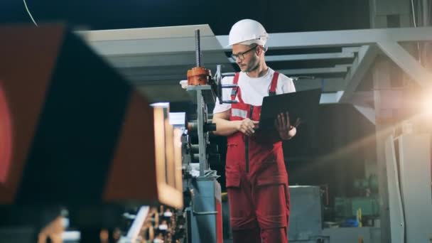 Vista lateral del ingeniero de pie con el ordenador portátil cerca del laminador — Vídeos de Stock