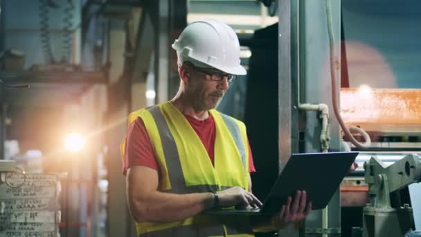 Engineer looking around and into laptop at sheet metal factory — Stock Video