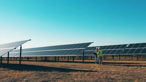 Drone tiro de três especialistas em energia solar que trabalham em uma fazenda solar — Vídeo de Stock