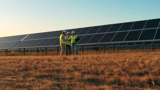 Três especialistas em energia solar tendo uma discussão em uma fazenda solar. Engenheiros profissionais discutem projeto inovador. — Vídeo de Stock