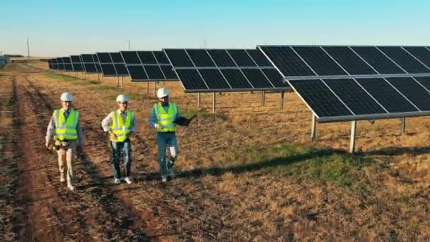 Três especialistas em energia solar caminhando em uma instalação de energia solar. Engenheiros profissionais discutem projeto inovador. — Vídeo de Stock