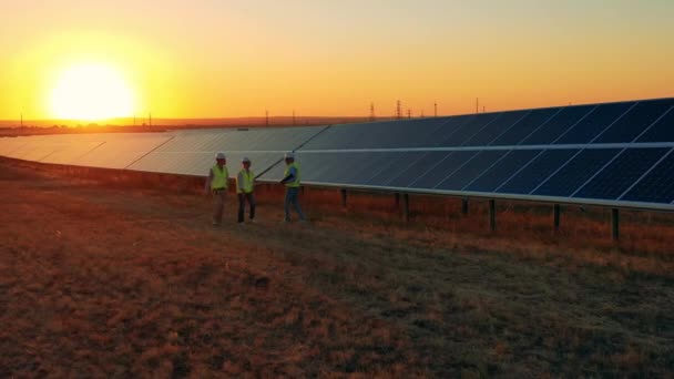 Tre specialisti di energia solare a piedi attraverso un parco solare al tramonto luminoso — Video Stock