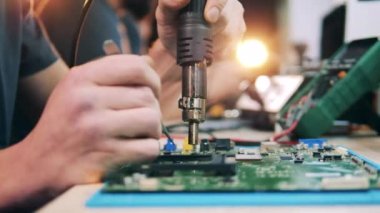 İşçi, ısı tabancası ve cımbız kullanarak sistem bileşenlerini lehimliyor
