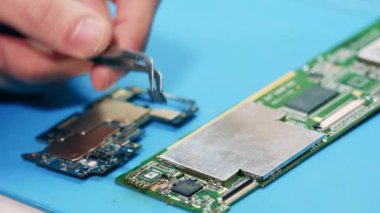 İşçi kırık parçaları devre kartından cımbızla çıkarıyor. Eller yukarı..