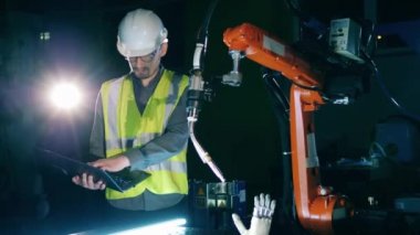 Güvenlik giysisi giyen erkek araştırmacı robot bir cihazı gözlemliyor, biyonik kol..