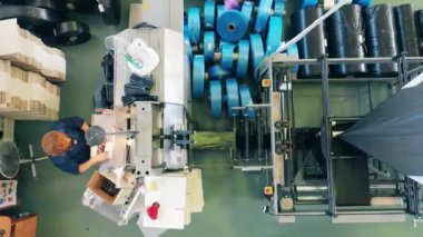 Kadın fabrika işçisi, üretim bandından bir kutuya siyah plastik poşetler dolduruyor.