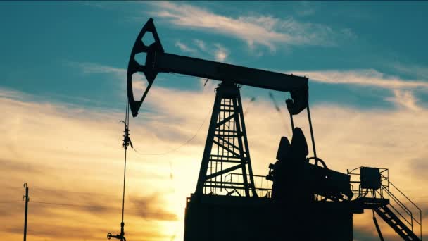 Dark silhouette of oil pumpjack in motion at golden hour — Video
