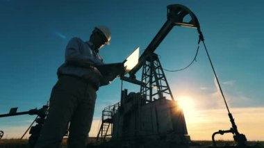 Petrol endüstrisi ekipmanlarına karşı dizüstü bilgisayarda yazan mühendisin düşük açılı görüntüsü