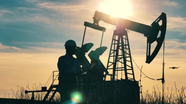 Engineer with laptop walking about oil pumpjack, drone flying — Stock Video