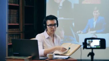 Kulaklık hocası işaretli kalemle bazı ders kitaplarına işaret ediyor.
