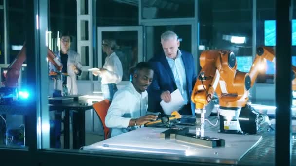Африканский мужчина наблюдает роботизированное устройство с группой инженеров — стоковое видео