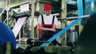 Erkek fabrika işçisi, dizüstü bilgisayarıyla plastik torba üretim sürecini izliyor.