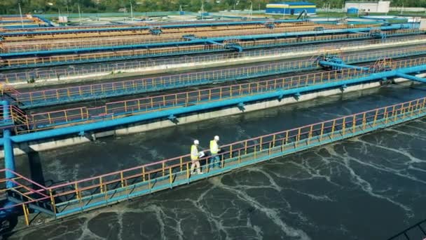 Drone shot of two specialists walking across the bridge at a water cleaning facility. Water management concept. — Stock Video