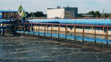 İki atık su operatörü su temizleme tesisinde borular boyunca yürüyorlar.