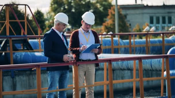 Due uomini d'affari che discutono di un sito di depurazione delle acque reflue alla luce del giorno — Video Stock