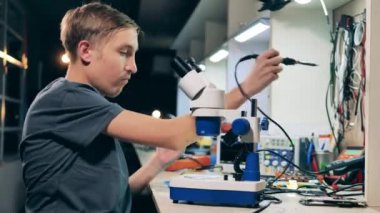 Erkek mühendis mikroskop kullanarak mikroskobu tamir ediyor.