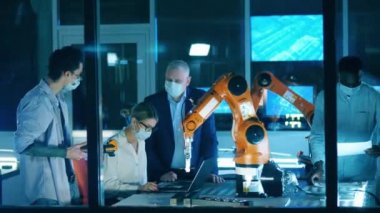 Maskeli mühendisler modern endüstriyel robotların yakınında fabrika otomasyonunun çözümlerini tartışıyorlar..