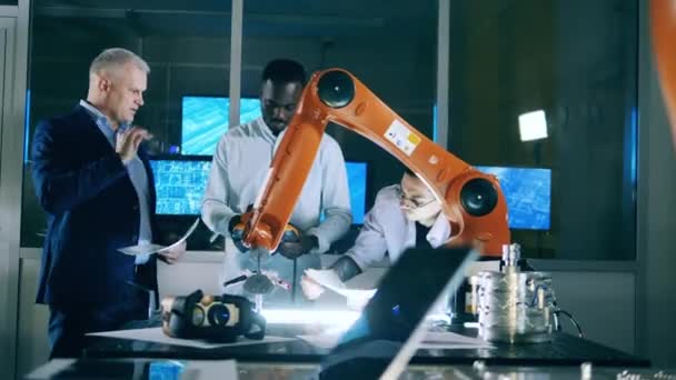 Inovasi, konsep teknologi. Tiga insinyur membahas masalah otomatisasi industri sementara robot menggambar — Stok Video
