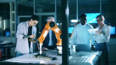 Endüstriyel robot mühendislerden oluşan bir ekip robot koluyla çalışıyor. Mavi ışıklı laboratuvarda robot performansını izleyen mühendisler