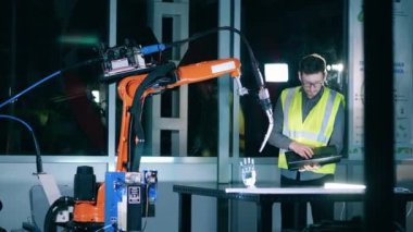 Dizüstü bilgisayarı olan mühendis endüstriyel robotik kolu kaynak için hazırlıyor.