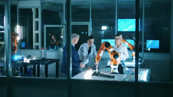 Drie ingenieurs bespreken industriële robot mogelijkheden in het laboratorium. Team van industriële robotica ingenieurs werken met robot arm. — Stockvideo