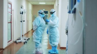 Tehlikeli madde giysisi giymiş iki doktor koridorda konuşuyor. Coronavirus, covid-19 pandemik konsept.