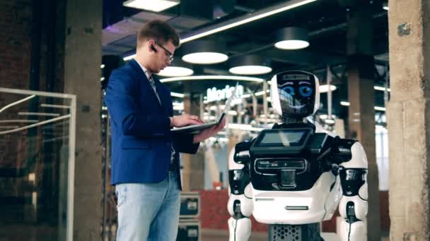Een man communiceert met een cyborg via een laptop. realistische robot ten dienste van de mens. — Stockvideo