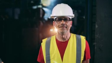 Kasketli ve çelik yelekli bir erkek uzman gülümsüyor.