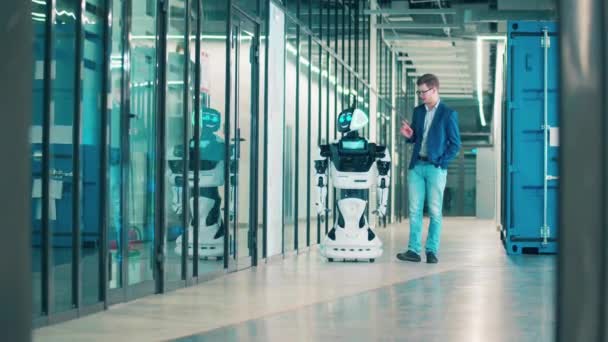Ein Mann und ein Roboter gehen den Flur entlang. Mensch und Roboter arbeiten zusammen. — Stockvideo