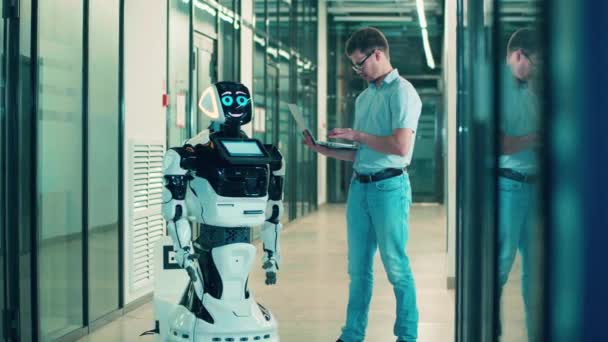 Mensch und Roboter arbeiten zusammen. IT-Spezialist steuert Cyborg mit Laptop — Stockvideo