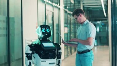 Bir adam robotla iletişim kurmak için dizüstü bilgisayar kullanıyor. Gelecekçi cyborg, yenilikçi robot konsepti.
