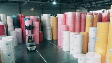Depoda büyük kağıt ruloları taşımak için forklift yükleyicisi çalıştıran bir işçi