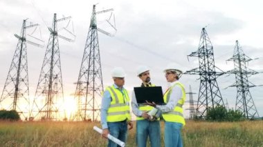 Elektrik santrali işçileri gün batımında bir elektrik santrali hakkında tartışıyorlar.