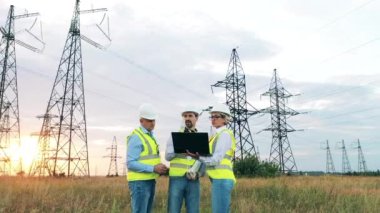 Üç fabrika işçisi bir dizüstü bilgisayar kullanarak bir enerji santralini inceliyor.