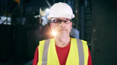 Metal üreten fabrika ünitesi ve kameraya bakan bir erkek çalışan.
