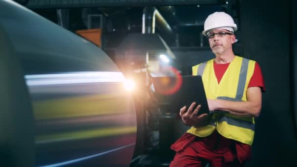 Especialista en metalurgia con un ordenador portátil está mirando a las máquinas de producción de metal — Vídeos de Stock