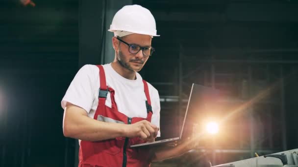 Hombre empleado está trabajando con un ordenador portátil y usando un hardhat — Vídeos de Stock