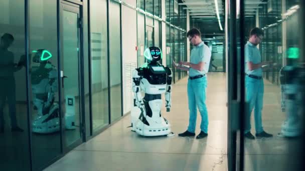 Un ingénieur avec un ordinateur portable gère une machine semblable à un robot — Video