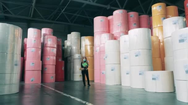 Trabajadora tomando notas en un almacén lleno de grandes rollos de papel — Vídeo de stock