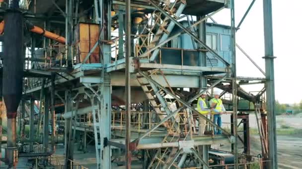 Construção industrial maciça com dois engenheiros em pé nela — Vídeo de Stock