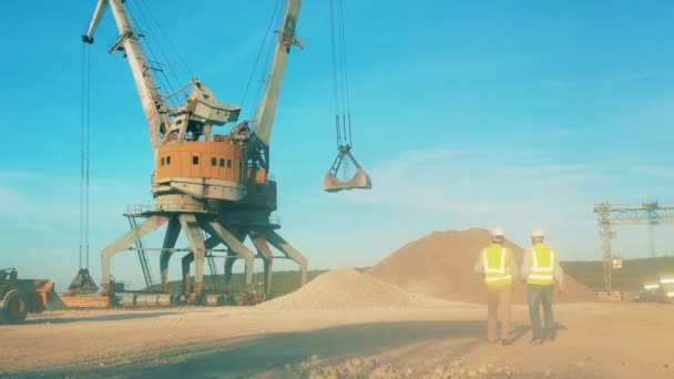 Zona de mineração com carregadores industriais e dois engenheiros andando por aí — Vídeo de Stock