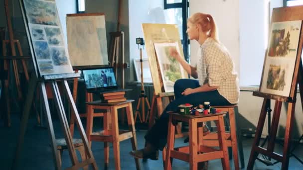 Een dame studeert schilderkunst online in het atelier — Stockvideo
