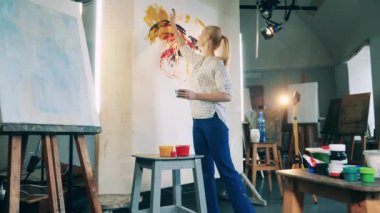 Sarışın kadın ellerini tuvale boyamak için kullanıyor.