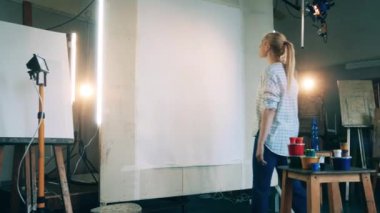 Bir bayan sanat stüdyosunda büyük bir tuvali inceliyor.