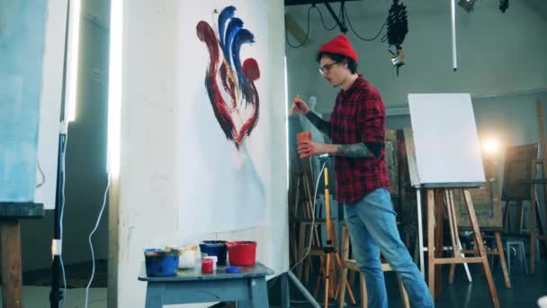 Een man schildert een schilderij op een groot doek met een kwast — Stockvideo